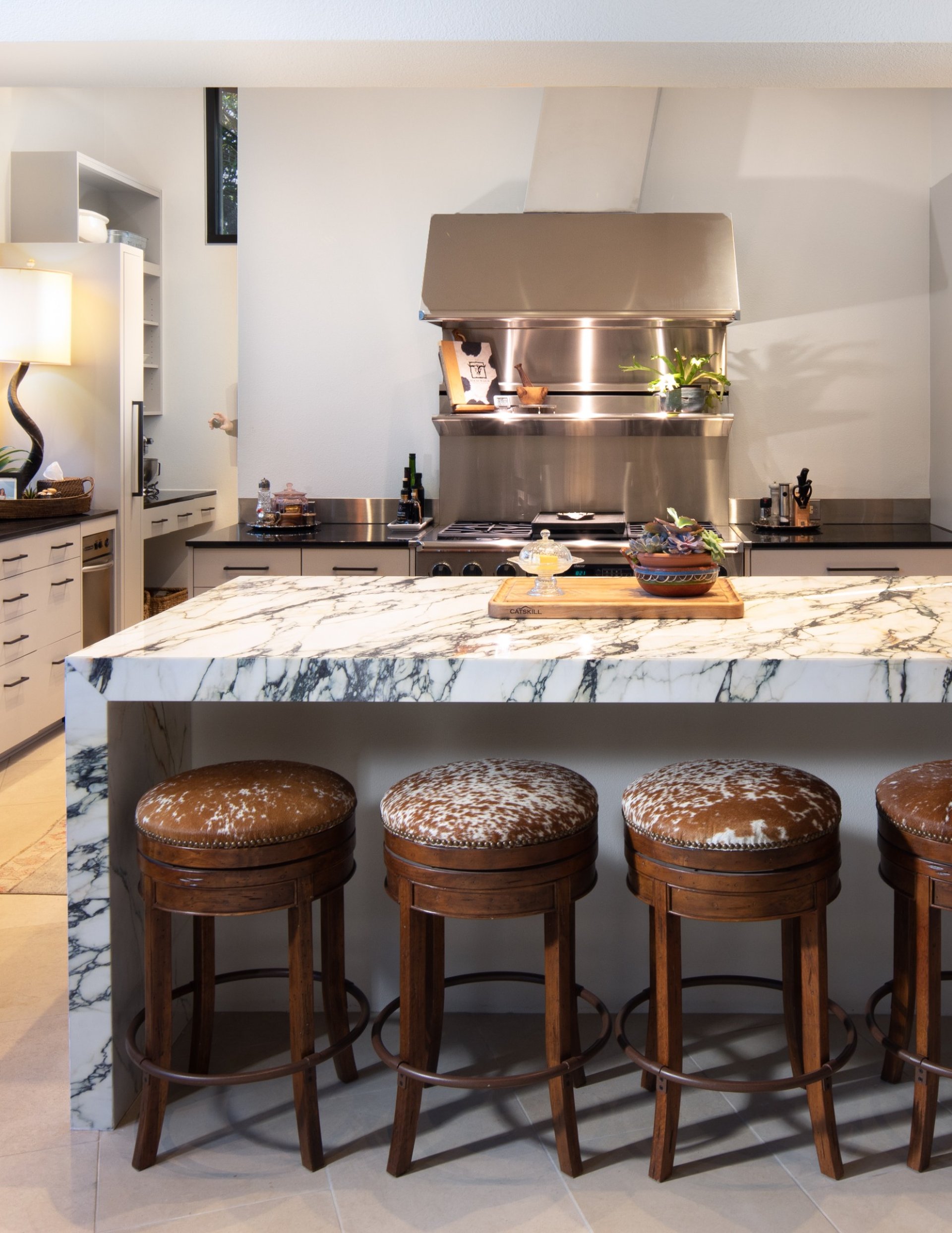 Luxury kitchen with marble waterfall island, cowhide bar stools, and professional stainless steel appliances – River City Construction and Design custom home.