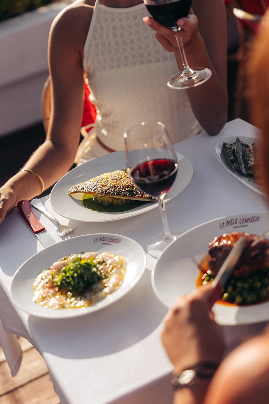 Deux personnes dégustant du vin rouge avec divers plats élégants sur table blanche.