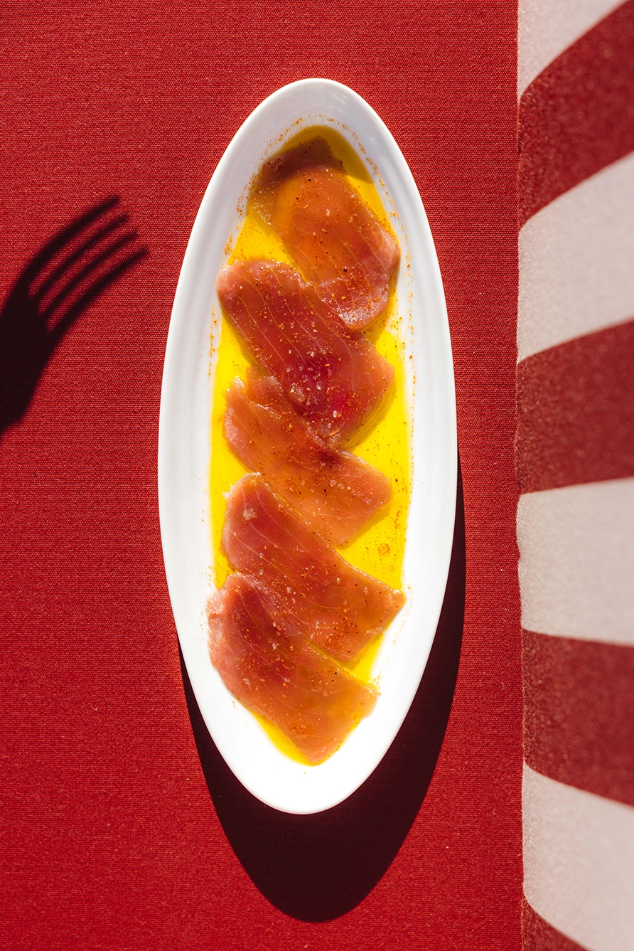 Tranches de poisson cru assaisonnées avec de l'huile et des épices sur une assiette blanche.