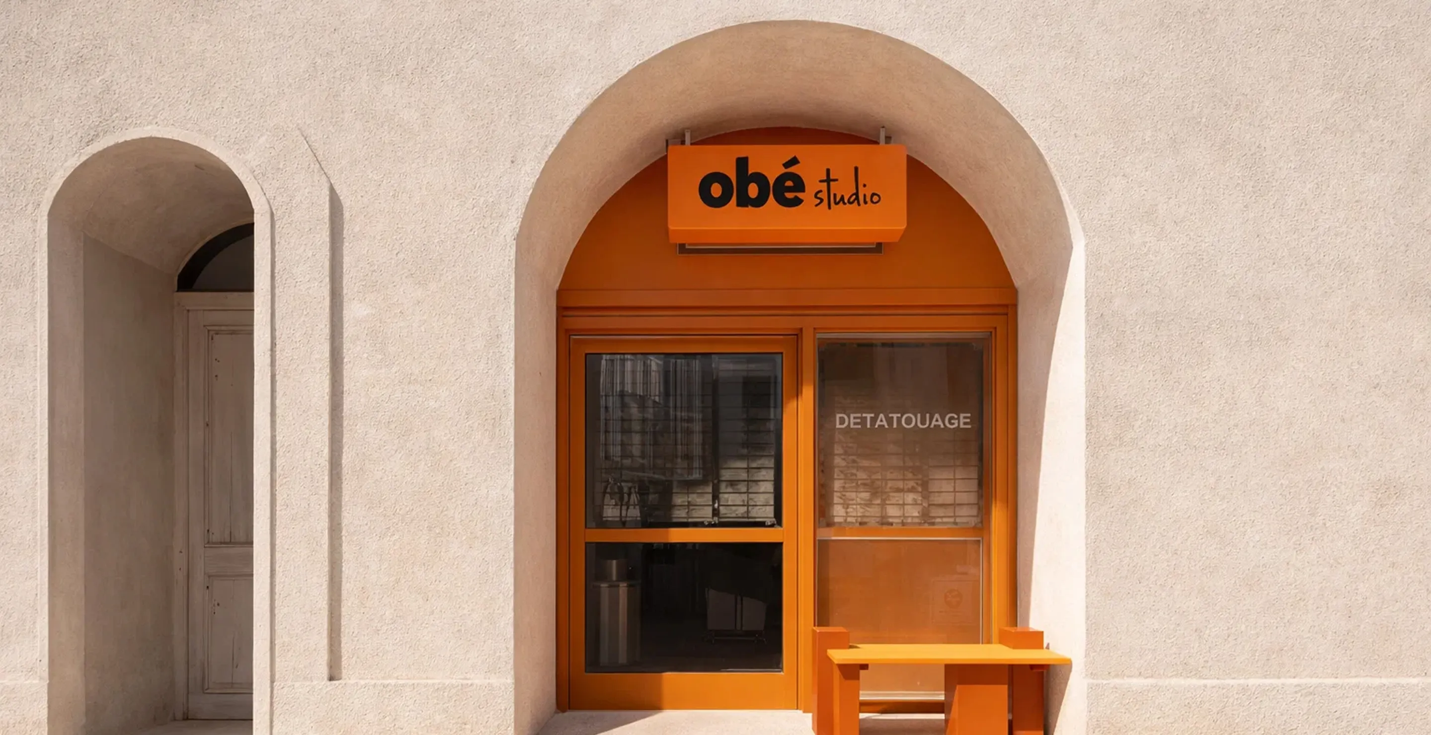 Orange arched storefront with an 'obé studio' sign and an orange bench outside.