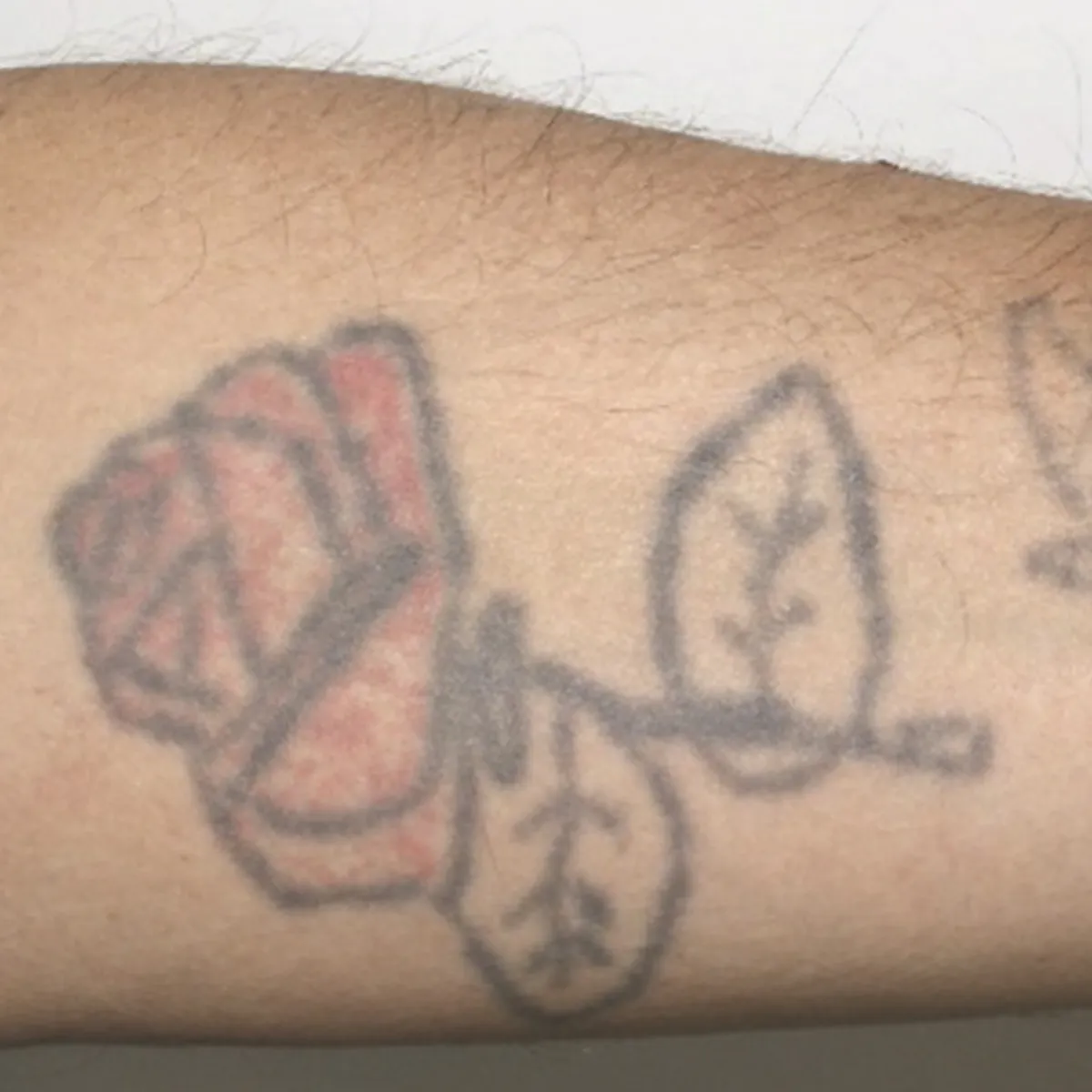 Tattoo of a red rose with two leaves on skin.