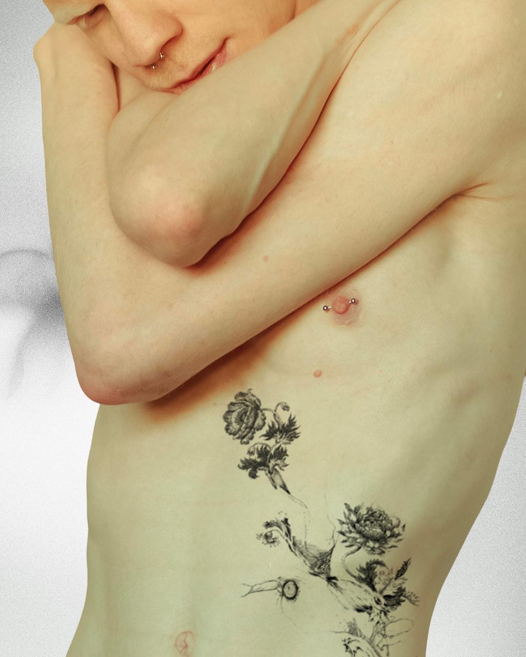 Close-up of a person's torso with arms crossed, showing a nipple piercing and a detailed black floral tattoo on the side.