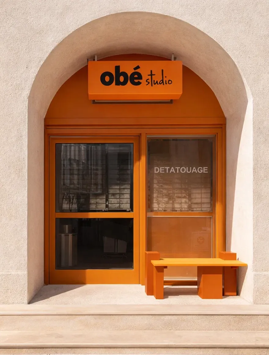 Orange-framed storefront with an arched beige entrance, an orange sign reading 'obé studio,' and an orange bench outside.