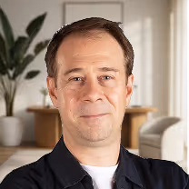 Portrait d'un homme aux cheveux courts bruns avec un léger sourire, en arrière-plan un salon lumineux avec des plantes et du mobilier moderne.