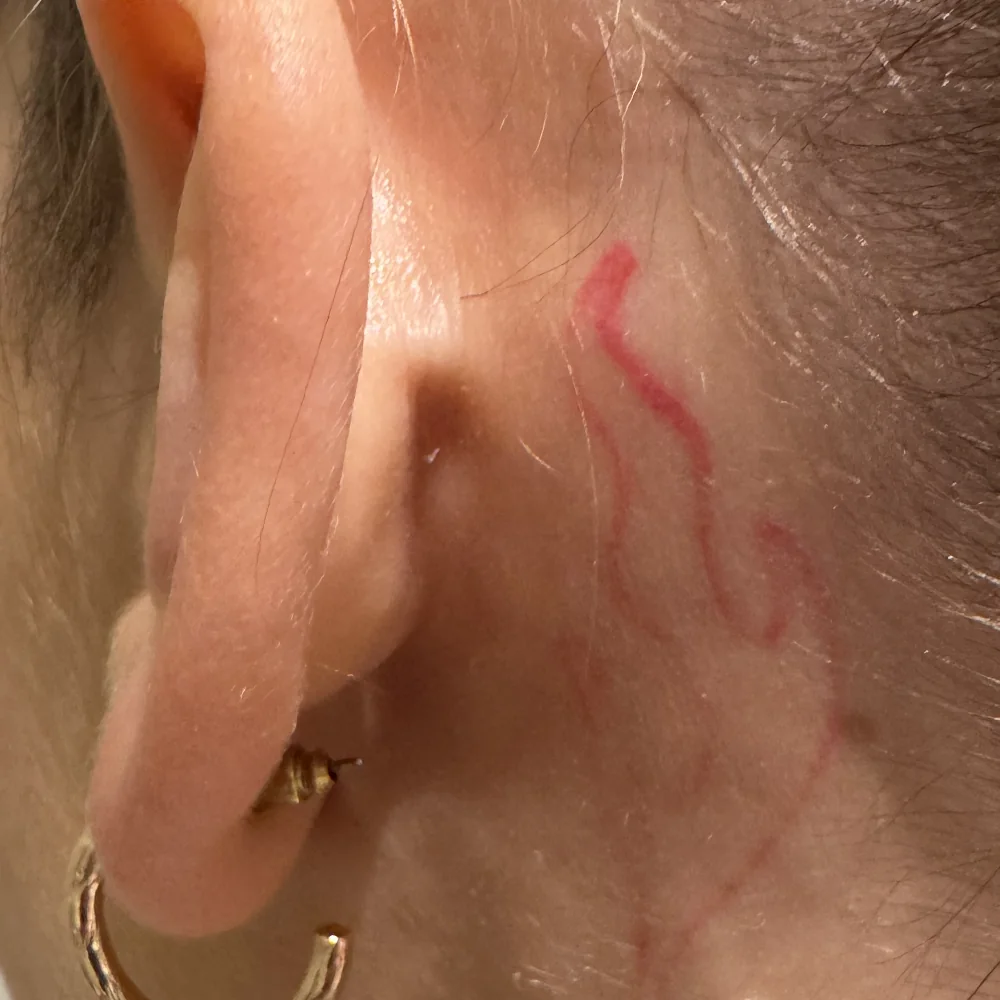 Tatouage à l'encre rouge derrière l'oreille avant détatouage laser chez obé studio à Marseille