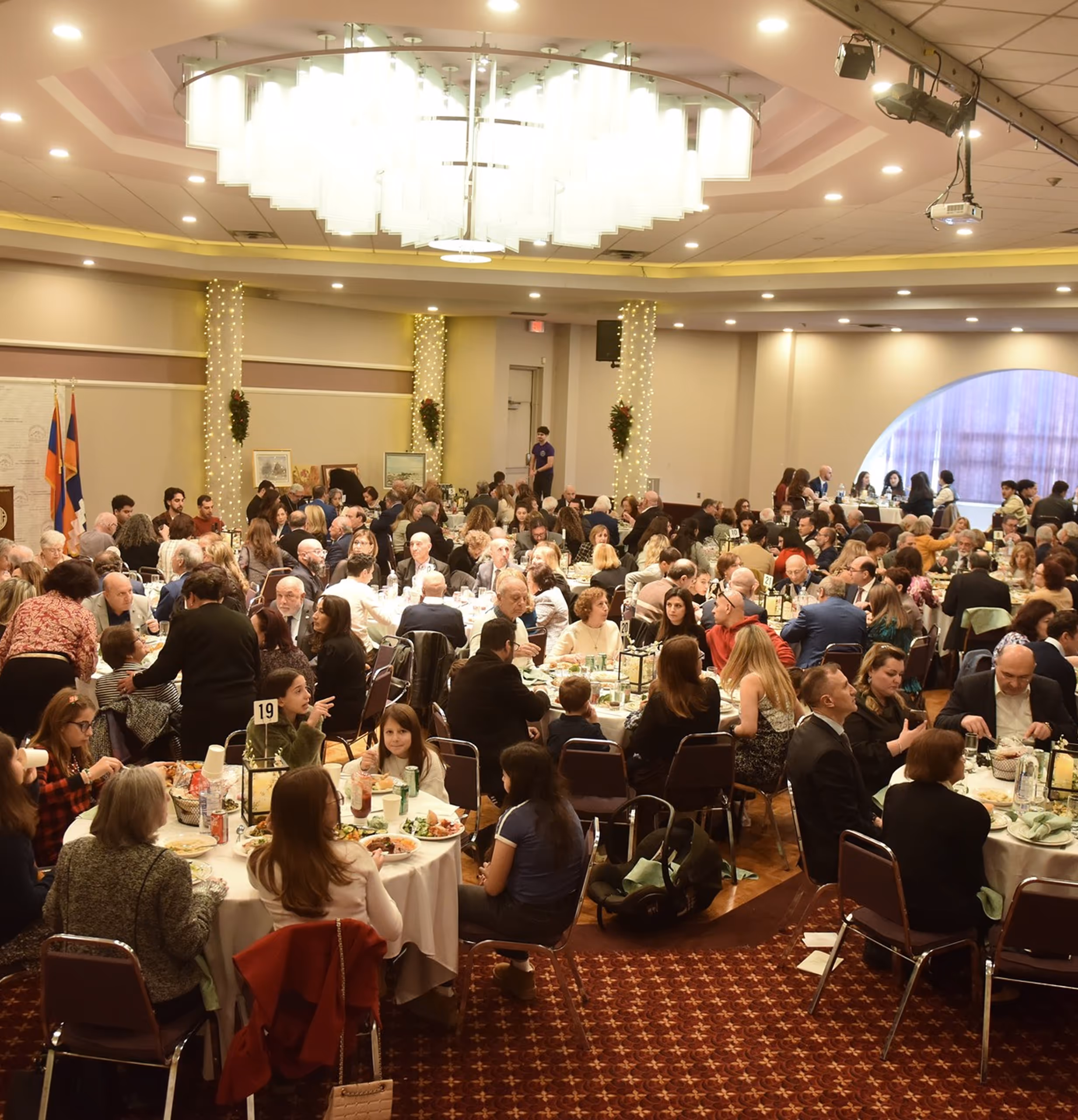 Large banquet hall filled with people seated at round tables enjoying a meal during an event.
