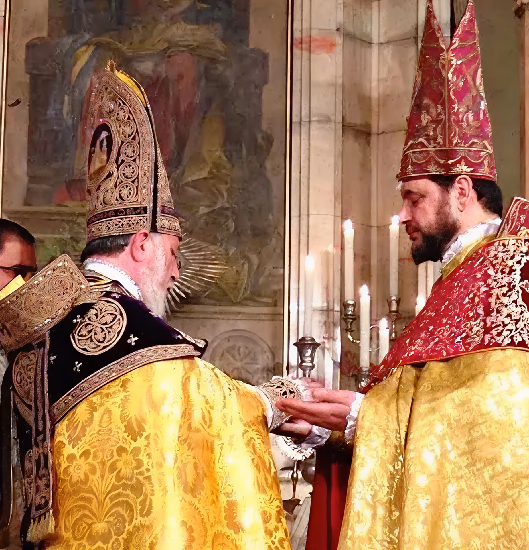 Two bishops in ornate ceremonial robes and miters holding hands during a religious ritual inside a church.