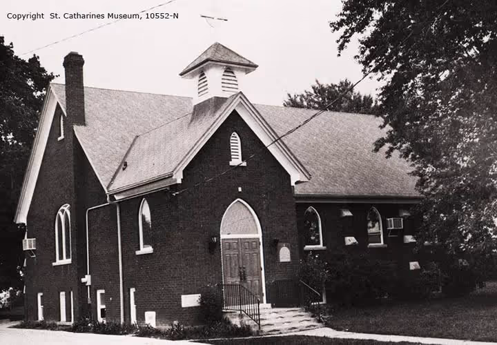 Black and white photo of a brick church building with arched windows and a small bell tower.