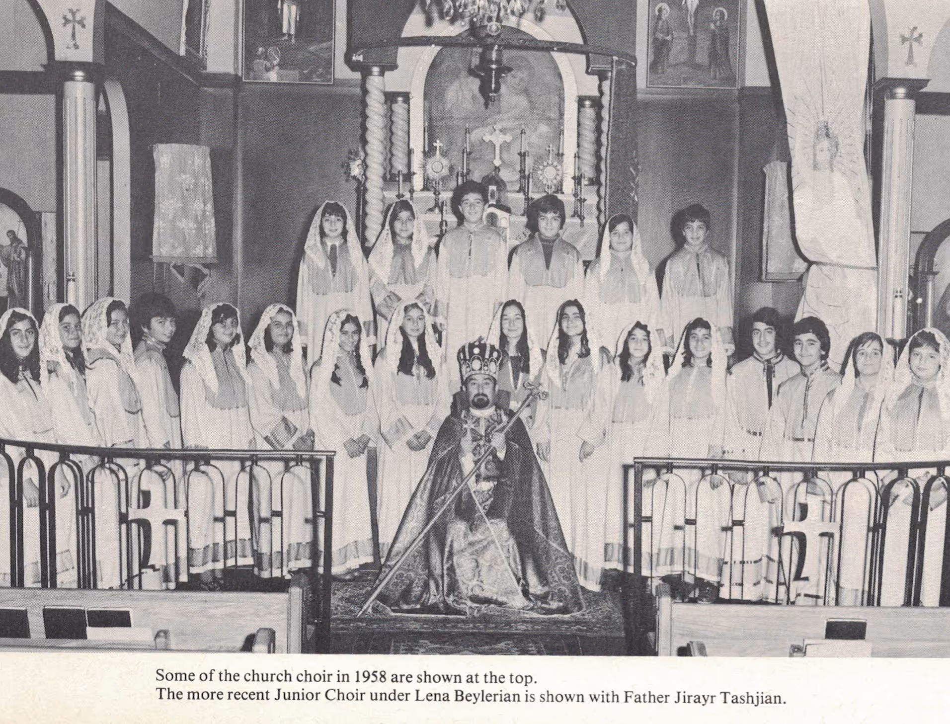 Black and white photo of a church choir with young boys and girls dressed in robes standing behind a seated priest in ceremonial robes and a crown inside a church.