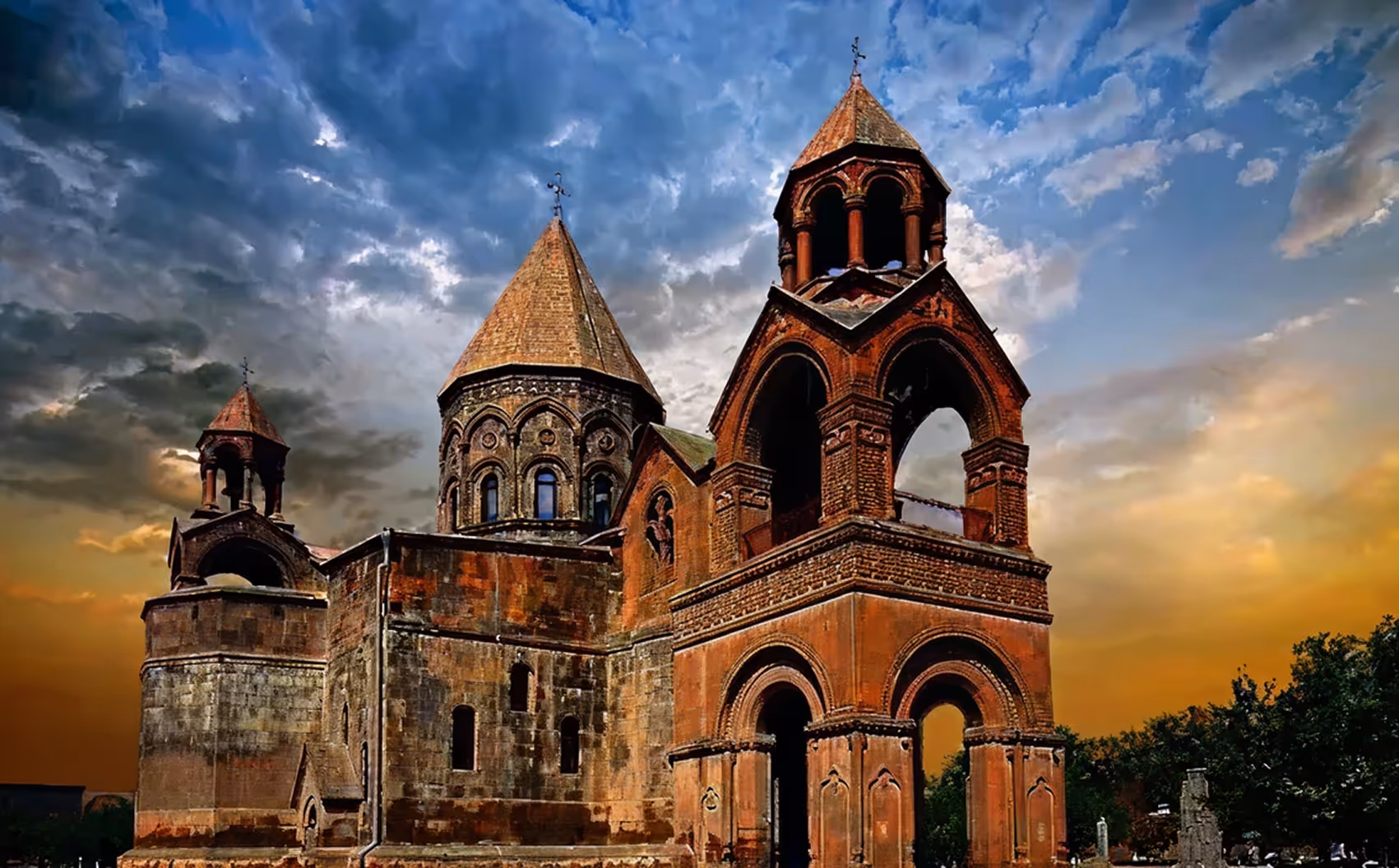Historic Armenian church with conical roofs and arches under a dramatic sunset sky.