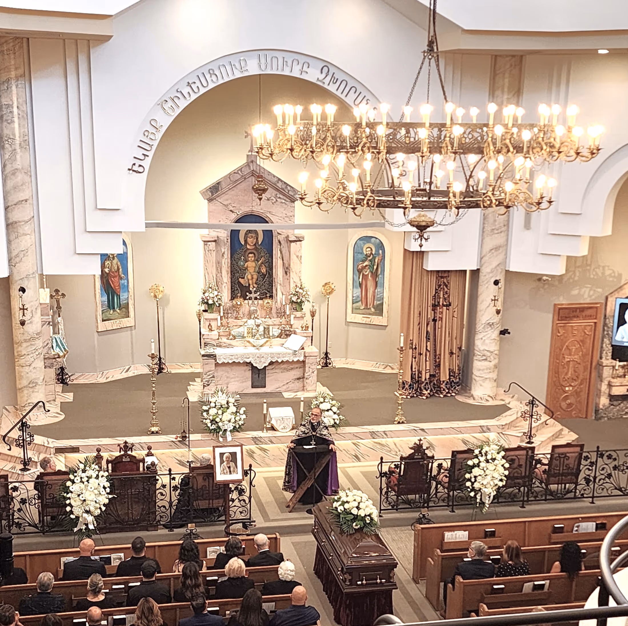 A funeral wreath of pink and white flowers with a ribbon reading “FROM VARTAN VARTANI AND FAMILY” inside Holy Trinity Armenian Church