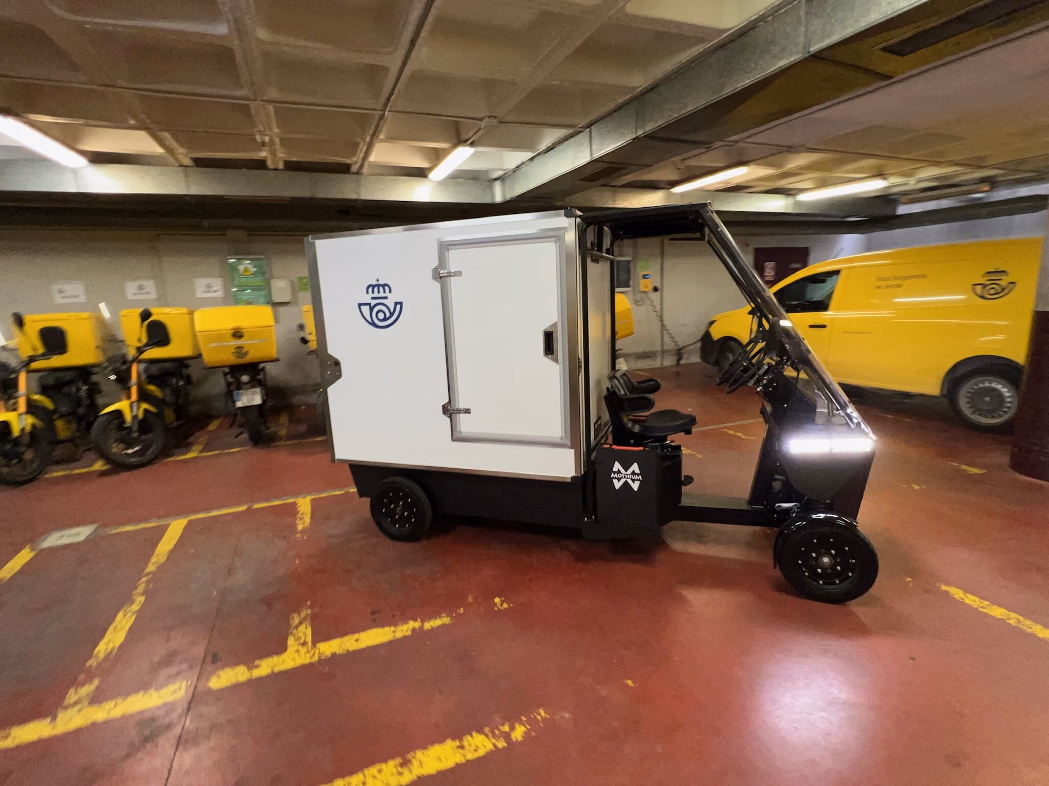 Mothium vehicle in a postal operator's depot, beside its scooters and van