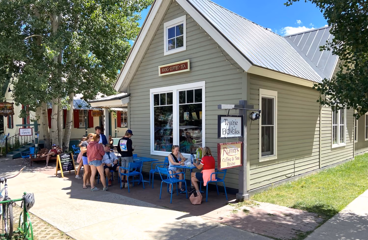 People sitting and standing outside Townie Books and Rumors Coffee and Tea House on a sunny day.