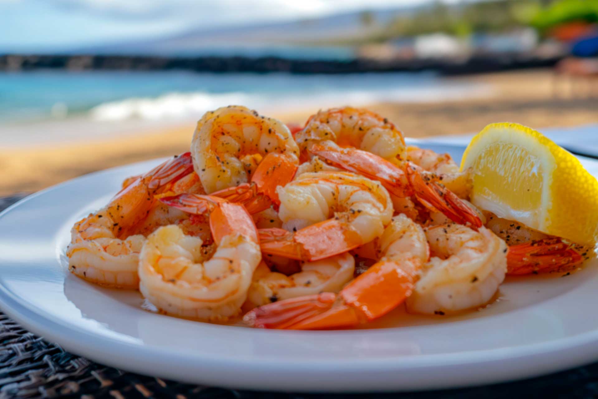 A plate of shrimp garnished with lemon wedges sits on a wooden table, ready to be served.