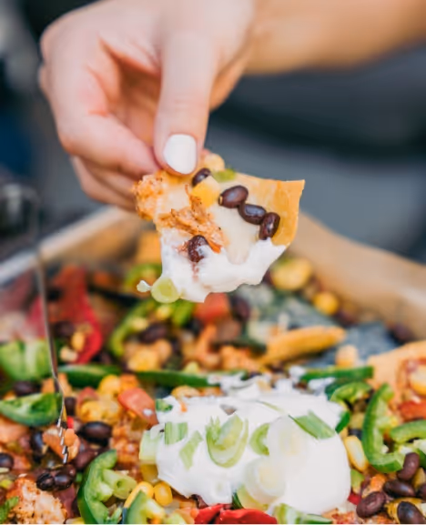 A person dipping a nacho chip into sour cream
