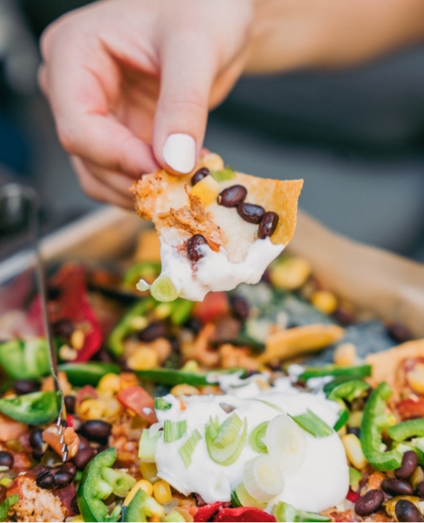 A person dipping a nacho chip into sour cream