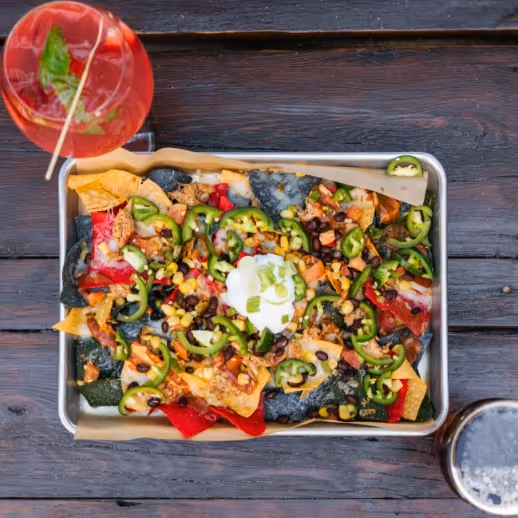 A top down photo of nachos on a table with a cocktail
