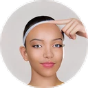 Young woman with clear skin wearing a white headband, pointing to her forehead with her index finger.