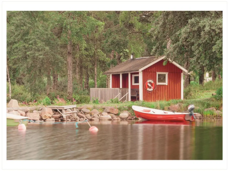 The shore of a lake with a small boat on the water and a cabin on land in the background