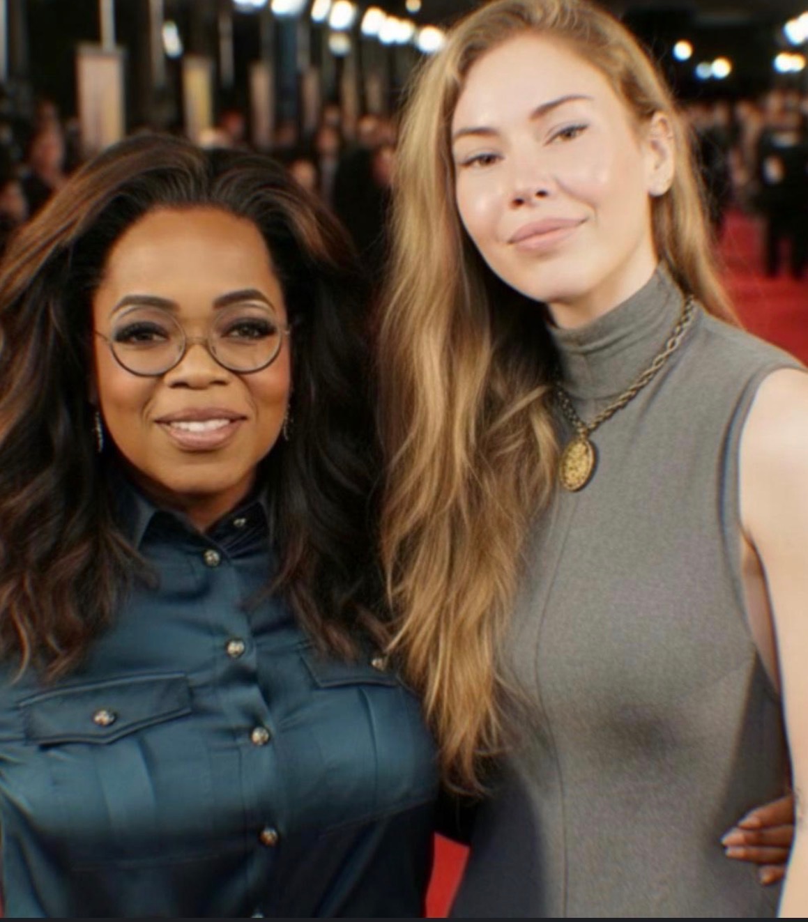 Two women smiling Sarah Marks and Oprah Winfrey at an event with a red carpet backdrop and lights overhead.