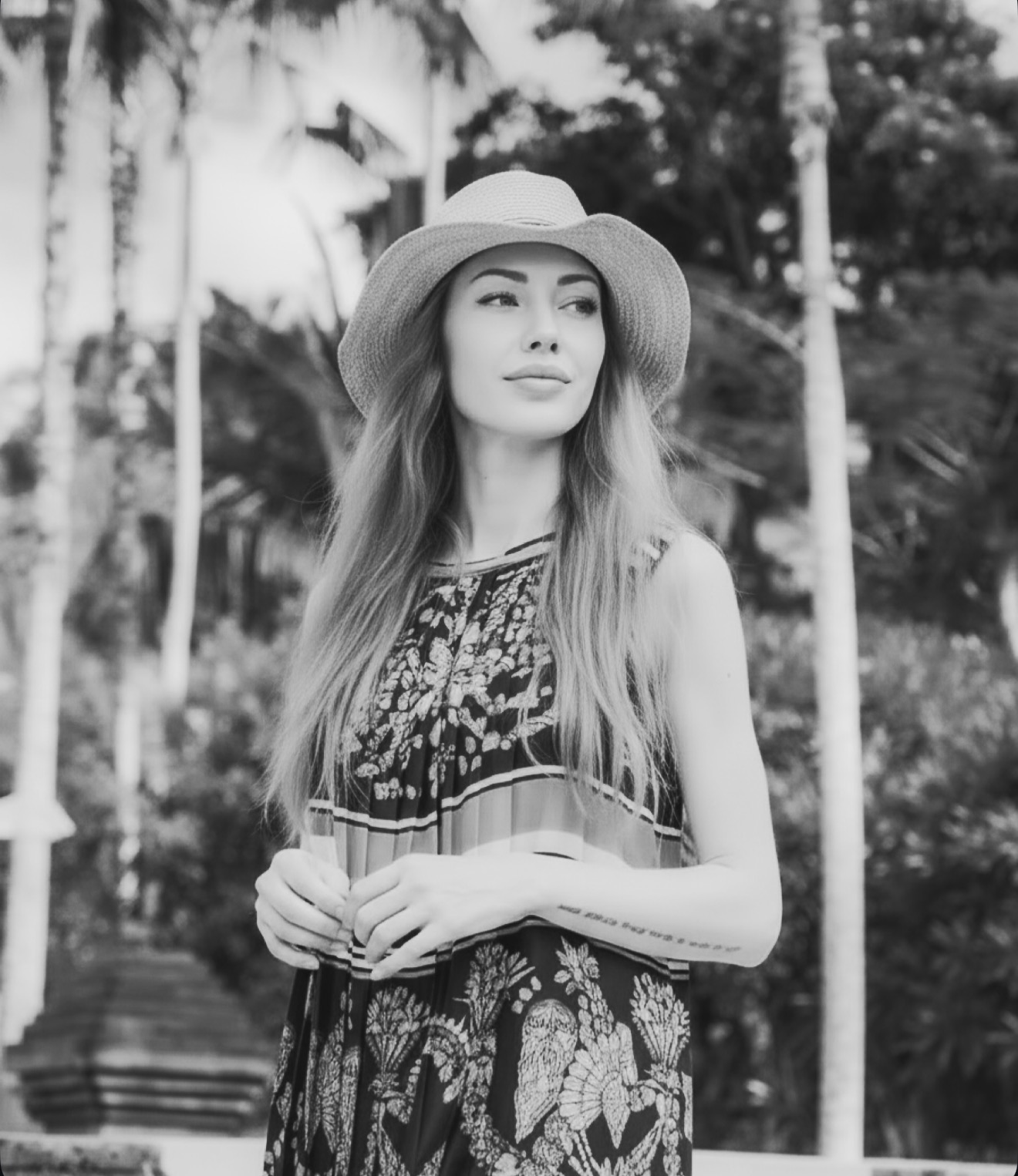 Sarah Marks wearing hat and patterned dress looking to the side outdoors with trees in the background.