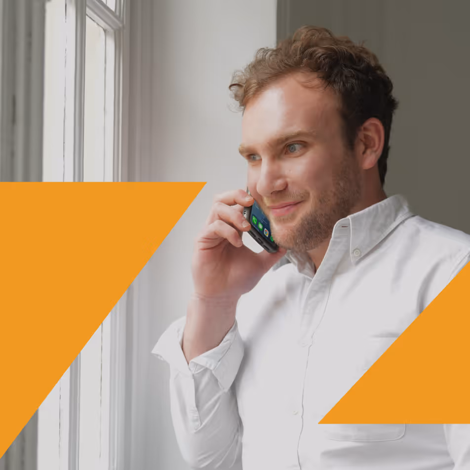 Homme souriant parlant au téléphone près d'une fenêtre avec chemise blanche et graphismes oranges.