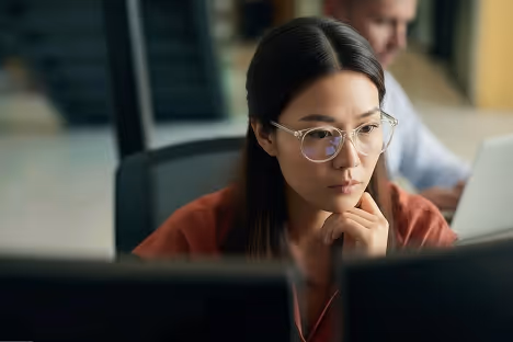 Focused woman wearing glasses working on a computer in an office.