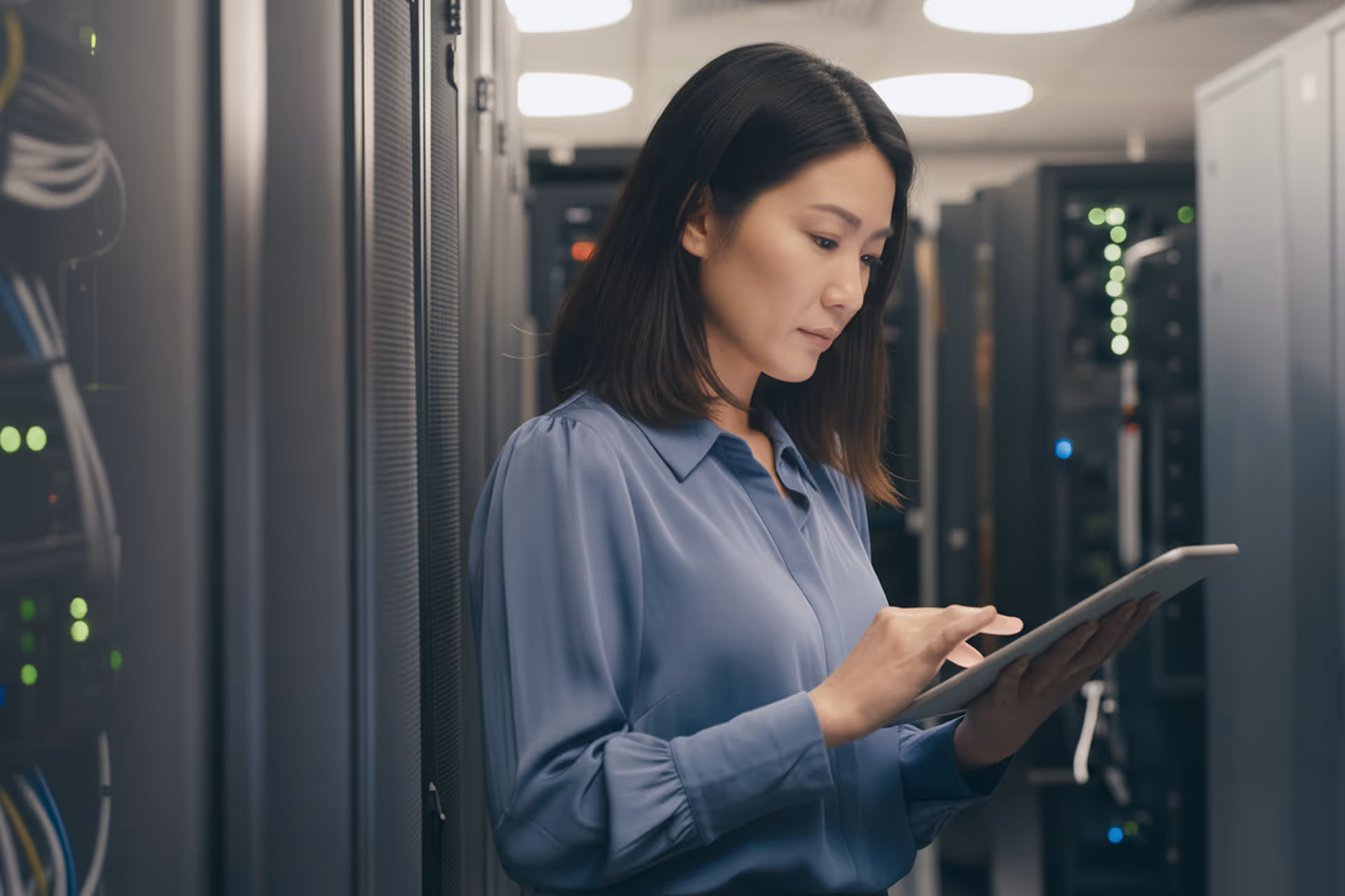 Woman in a server room using a tablet to monitor or manage network equipment.