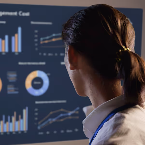 Person with hair tied back looking at a screen displaying colorful charts and graphs including bar charts, line graphs, and a donut chart.