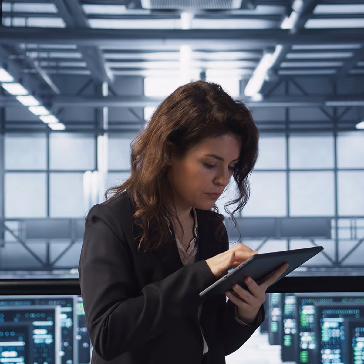 Woman in business attire interacting with a tablet in a modern data center.