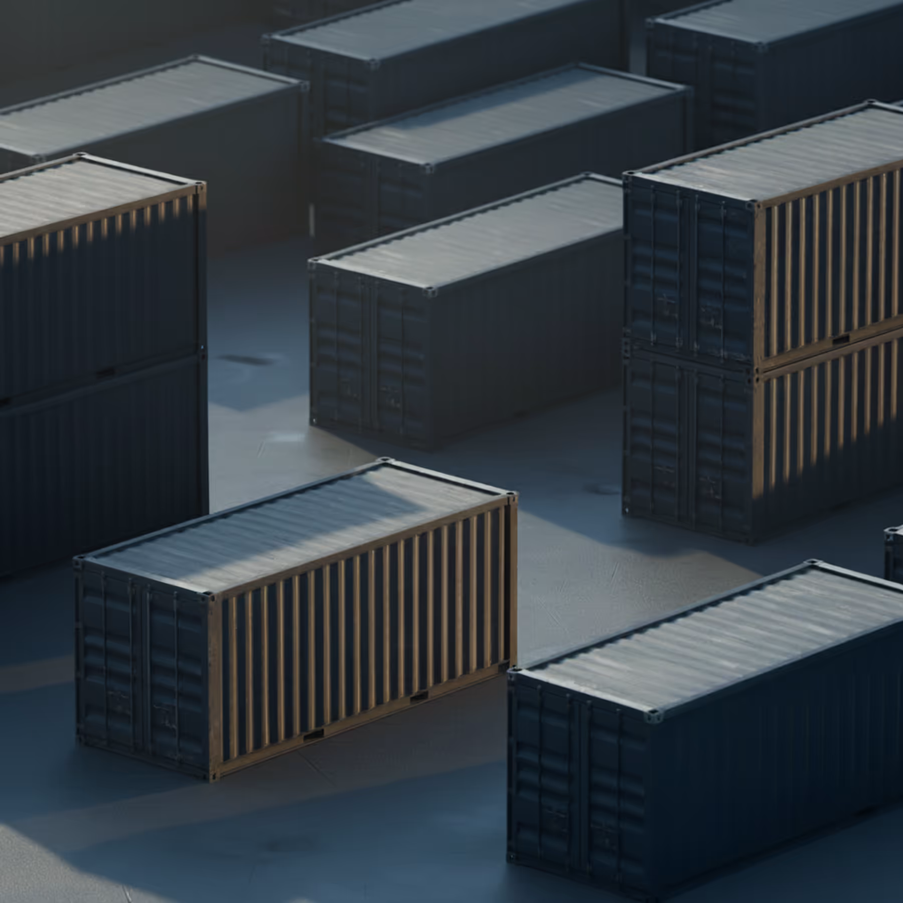 Cluster of dark shipping containers arranged on a concrete surface with sunlight casting shadows.
