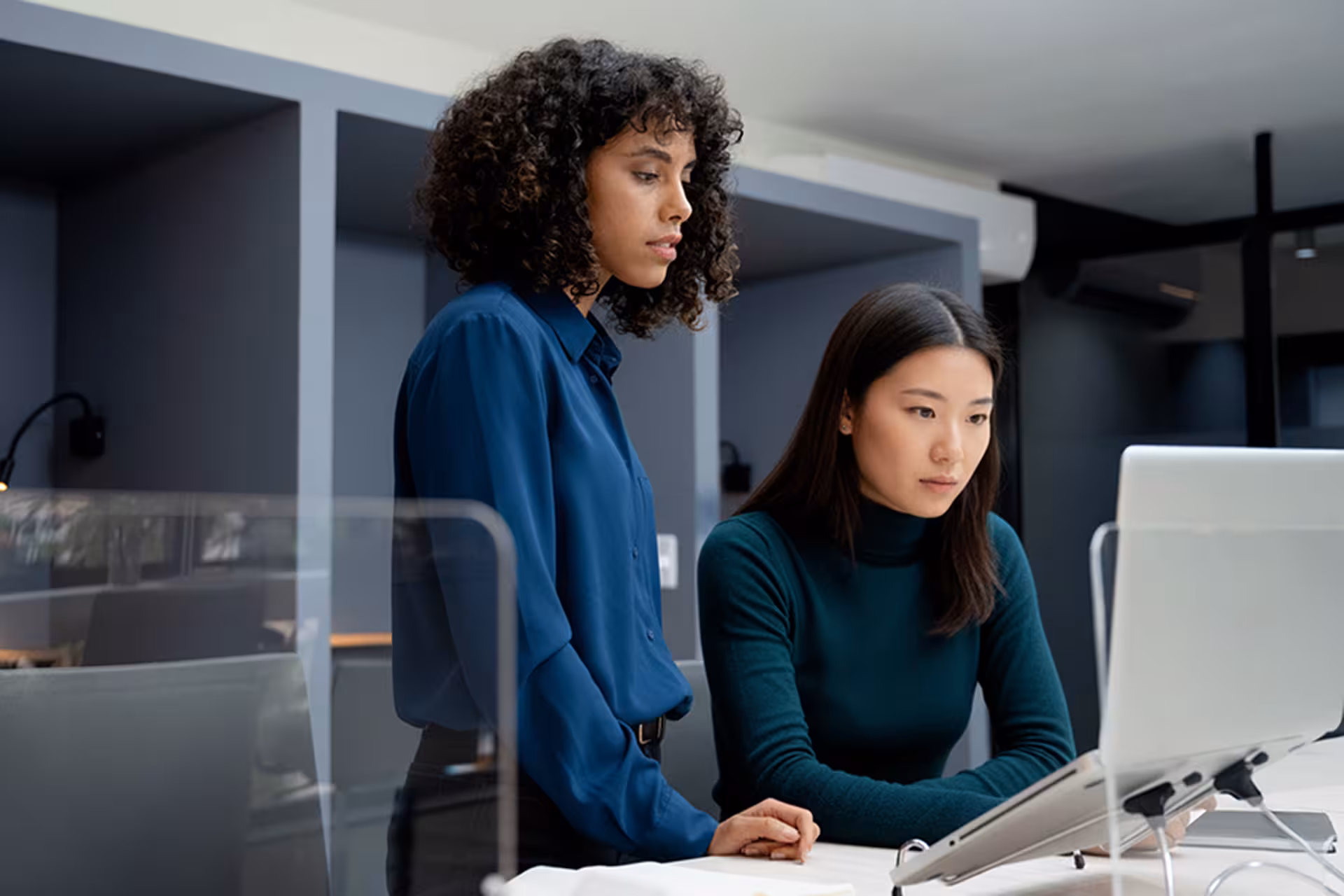 Two professional women working together and focused on a laptop in a modern office.