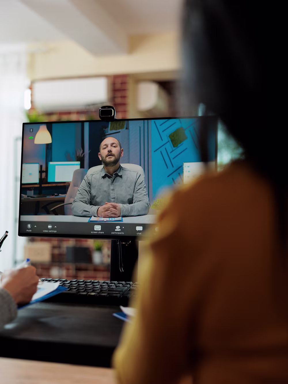 Person attending a video conference with a man on a computer screen sitting at a desk.
