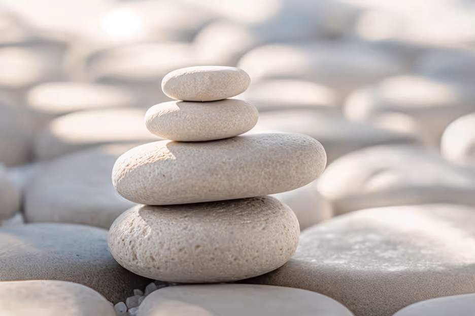 Stack of four smooth, light-colored stones balanced on each other with blurred stones in the background.