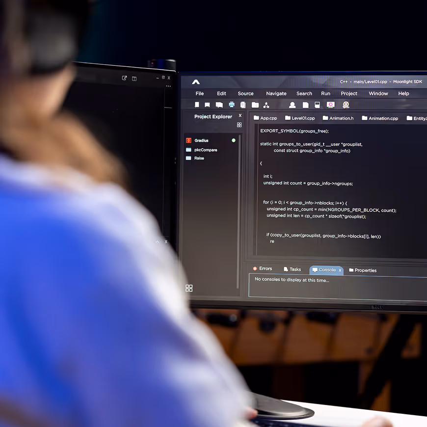 Person wearing headphones working on a computer with code displayed on screen in a dark room.