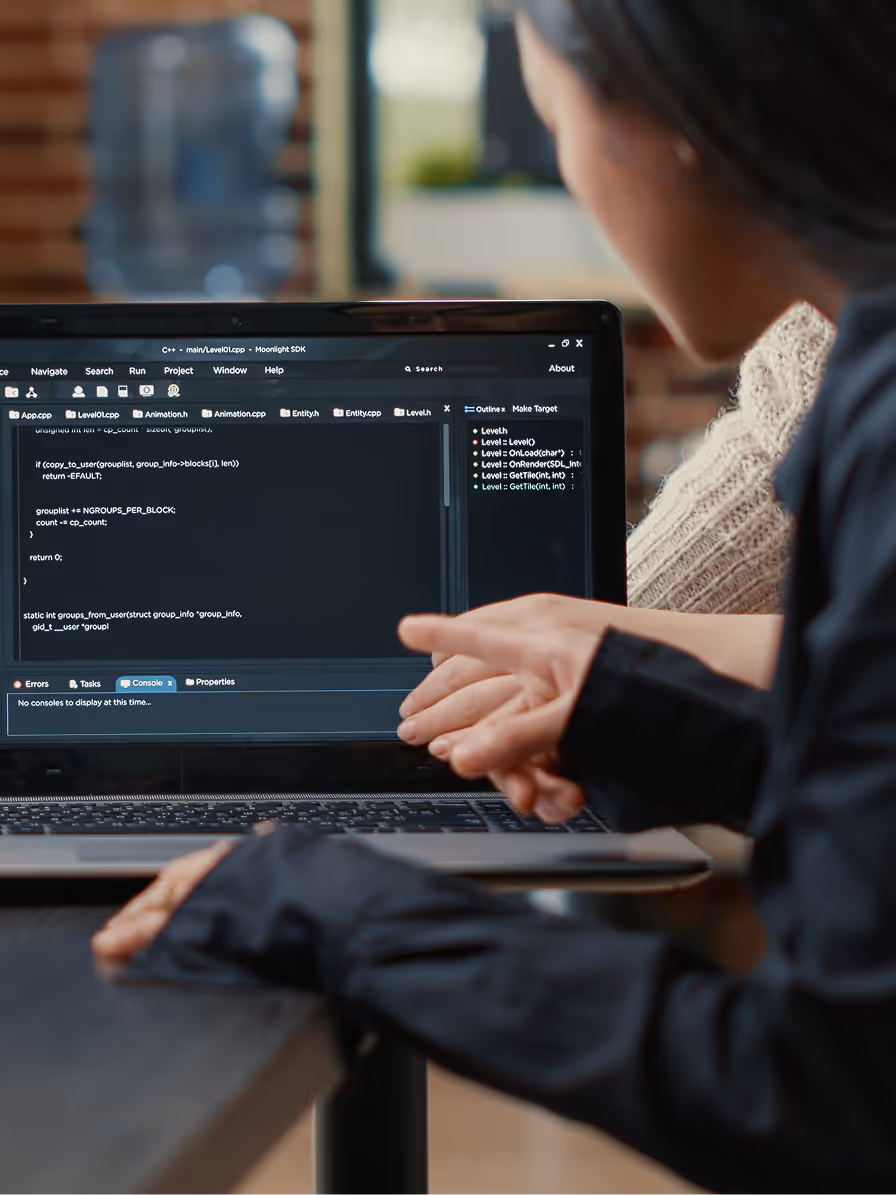 Person gesturing with hands while looking at a laptop screen displaying C++ code in a development environment.