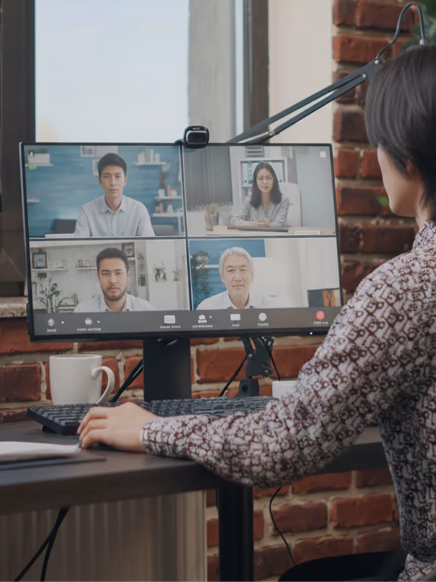 Person attending a video conference call on a computer showing four participants on the screen in a home office.