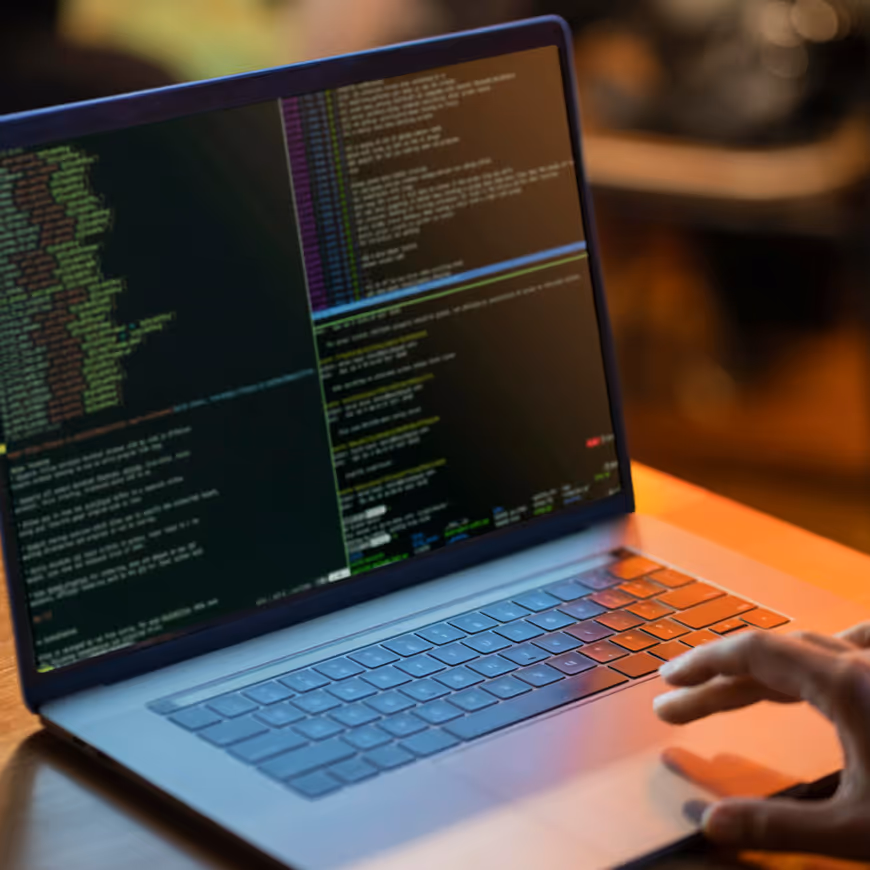 Laptop displaying multiple panes of code on the screen with a hand poised above the keyboard.