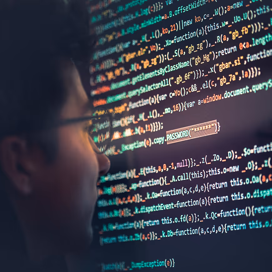 Person wearing glasses looking at a computer screen filled with colorful programming code including the highlighted word PASSWORD.