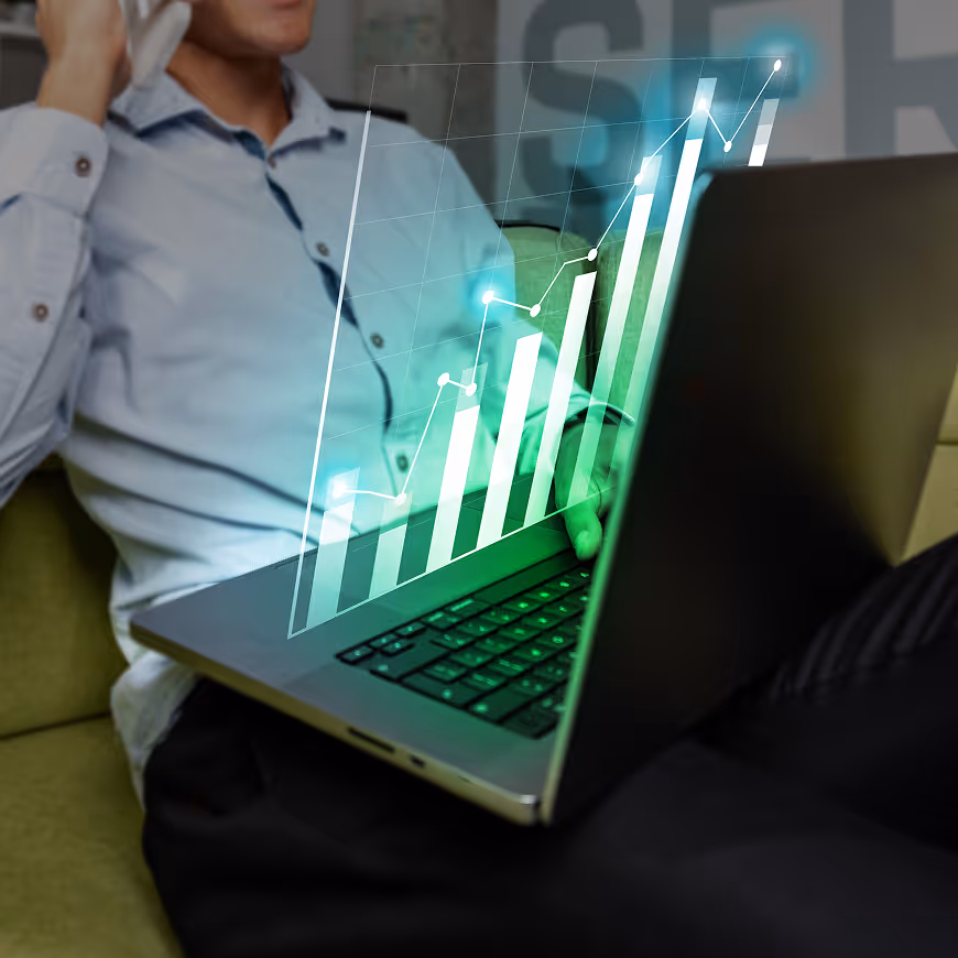 Person sitting on a couch using a laptop with a holographic rising bar graph projection above the keyboard.
