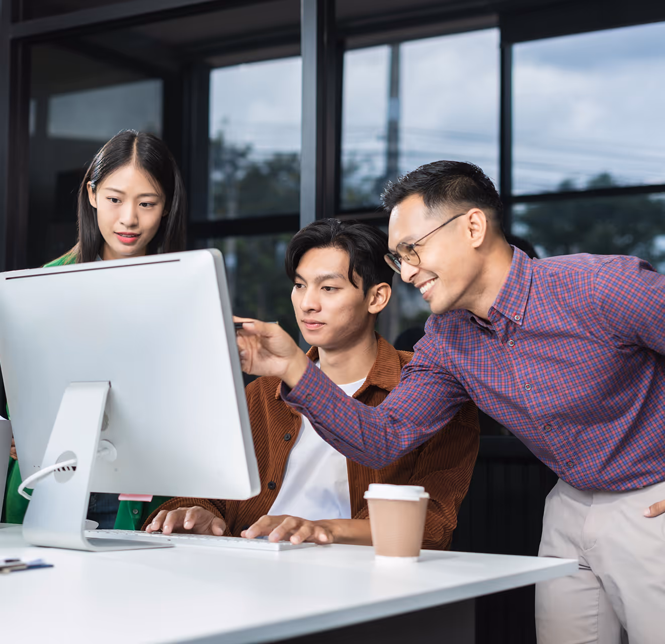 Three colleagues collaborating and looking at a desktop computer screen in an office setting.