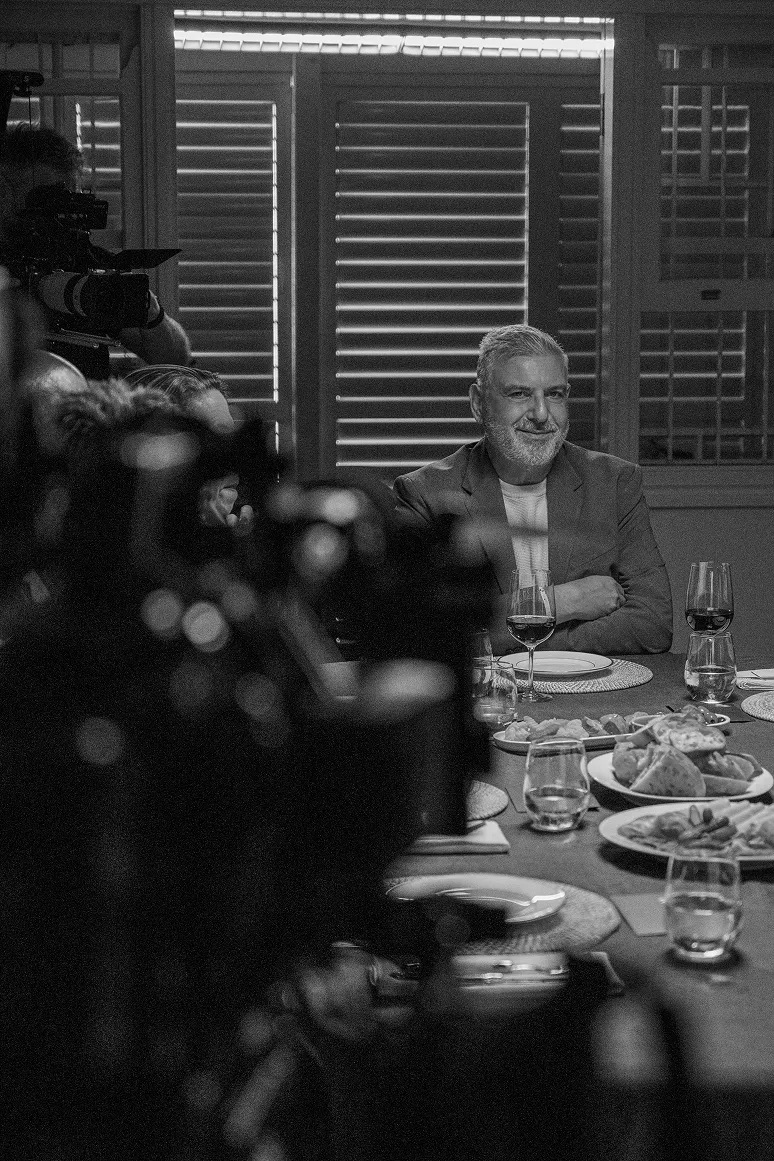 The image of The Seventh Seat shows host Steve George Makris seated at dinner table.