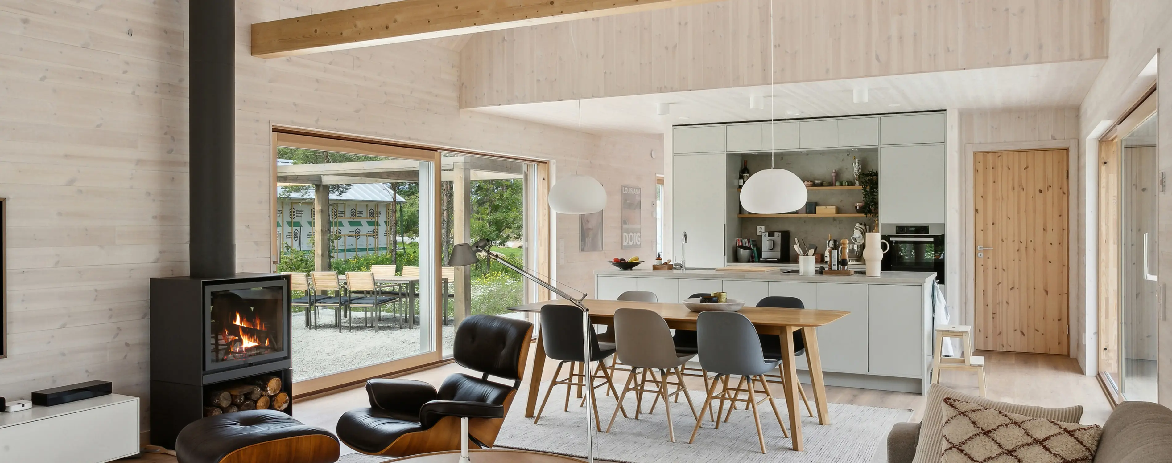 Scandinavian-style living room with a fireplace, wooden dining table, and open kitchen with large windows.