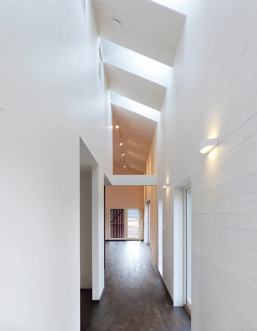 Bright, modern hallway with high ceilings, angled skylights, and white walls allowing natural light to stream in.