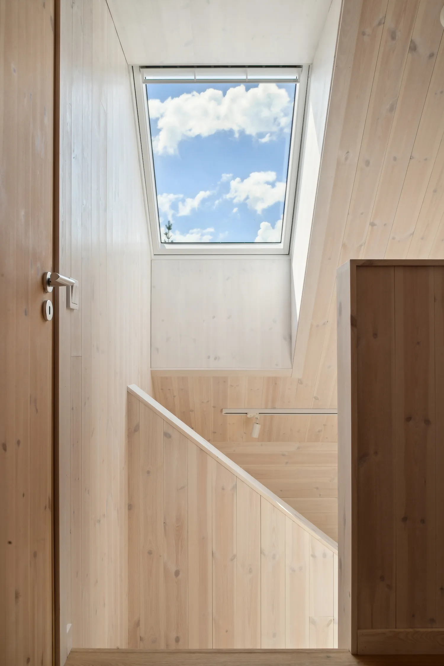 Interior staircase in the Arvesund house model Lit, with light wood walls and ceiling, and a skylight framing the blue sky and clouds.