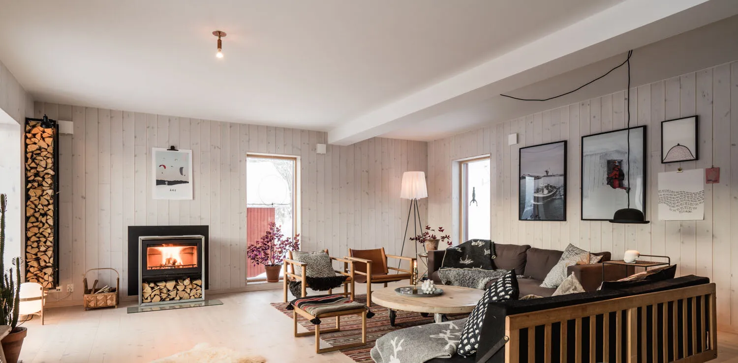 Living room in the Arvesund house model Hara, with a modern fireplace, wood storage, Scandinavian furniture, and light wooden walls creating a warm and inviting atmosphere.
