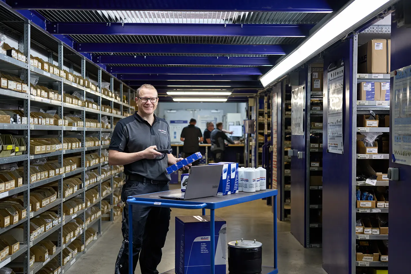 Mitarbeiter im Ersatzteillager von Heinr. Schmidt in Paderborn scannt Fahrzeugteile und arbeitet am Laptop zwischen Regalen.