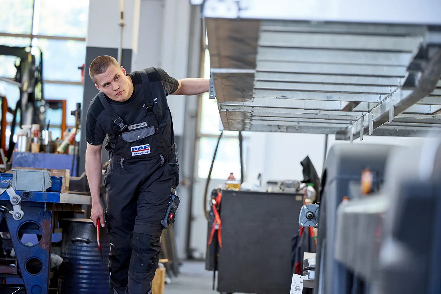 Mechaniker bei Heinr. Schmidt in Paderborn prüft einen Lkw-Aufbau in der Werkstatt und inspiziert sorgfältig die Unterkonstruktion.