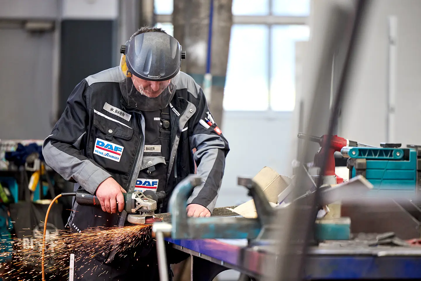 Handwerker schleift Metall mit Winkelschleifer und erzeugt Funken in einer Werkstatt.