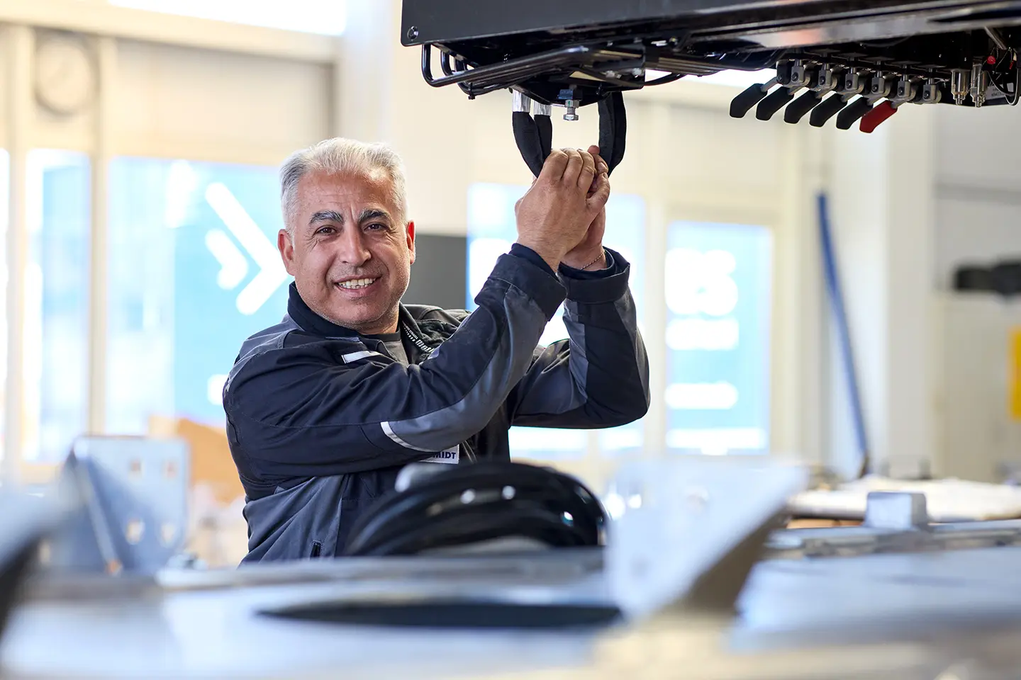 Ein Mann in Arbeitskleidung lächelt, während er an einem Industriegerät arbeitet.